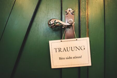 Closed green wooden doors with decorative fittings. On handle hanging white sign "Wedding, please do not disturb!" Wedding day concept.の写真素材