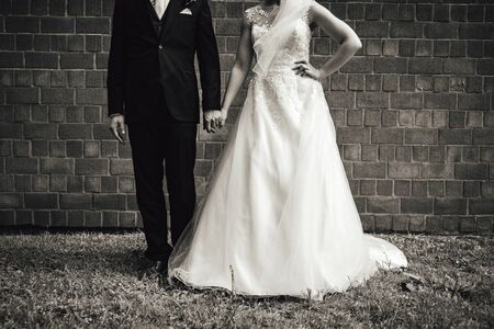 Black and white photo of wedding couple. Bride and groom in standing at brick wall. Bride posing with hand on her hip. Without head. Wedding dayの写真素材