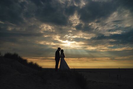 Distant view of marriage pair silhouette on evening beach. Dramatic sky with sun rays among clouds...
