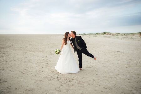 Newlyweds standing and kissing each other on sandy beach. Bride and groom posing. Wedding day concept.の写真素材