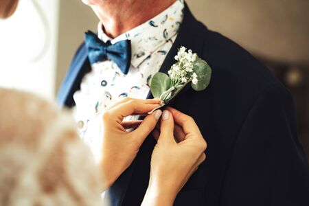 Close up female hands attaching wedding boutonniere on mans suit. Small posy on lapel of jacket. Wedding day concept.の写真素材