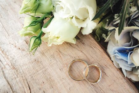 Top view up of couple of wedding rings laying on rough wooden table. White wedding bouquet on side. Wedding day concept.の写真素材