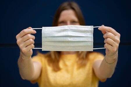 Woman holding disposable surgical face mask in outstretched hands in front of her face. Focused on mask. Corona virus pandemic protection concept.の写真素材
