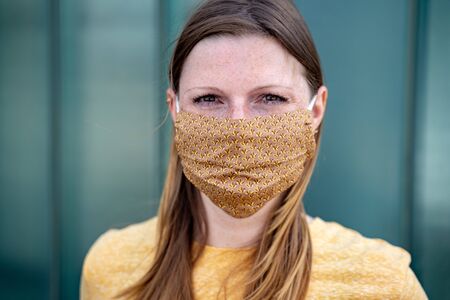 Head shot of woman wearing fashionable textile face mask. Handmade colorful protective mask with...