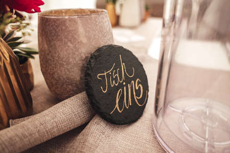 Closeup of table decoration. Rough table cloth in natural colors. Ceramic utensil and black round...
