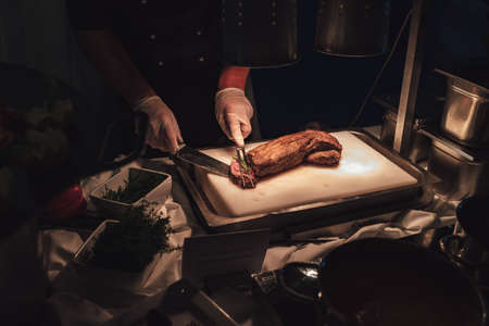 Man slicing piece of grilled beef filet meat on white kitchen board and serving it with rosemary. Celebration, party, birthday or wedding concept.の写真素材