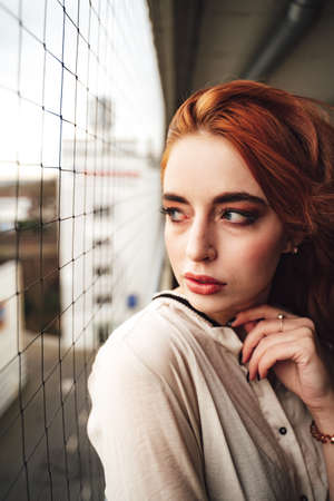Portrait of pretty millennial woman with elegant long red hair. Young female model looking to side over her shoulder through safety net.の写真素材