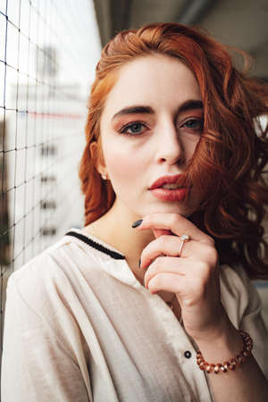 Portrait of attractive red haired girl with perfect make-up. Pensive young female model touching her chin and looking to camera.の写真素材