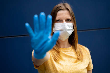 European woman wearing protective face mask, outstretched hand with protection glove as stop symbol. Corona virus pandemic protection concept.の写真素材