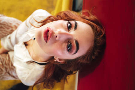 Beautiful caucasian girl sitting on yellow railing and looking to camera. Female red haired model in long skirt.の写真素材
