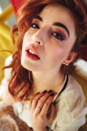 Beautiful caucasian girl sitting on yellow railing and looking to camera. Female red haired model in long skirt.の写真素材