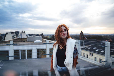 Portrait of smiling beautiful millennial girl standing on lookout terrace. Attractive young woman in jacket looking to camera.の写真素材