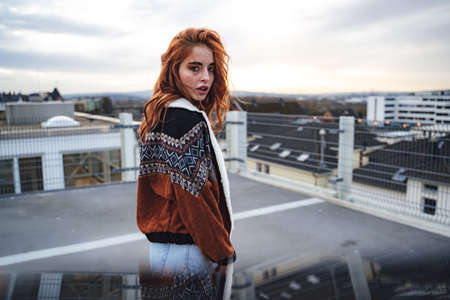 Portrait of beautiful girl with long red hairs looking to camera. Model wearing jacket. Outdoor photo, overcast weather.の写真素材