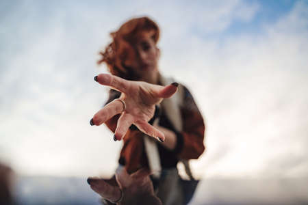 Closeup of fingers of outstretched young woman hand to camera. Female model against sky. Black...