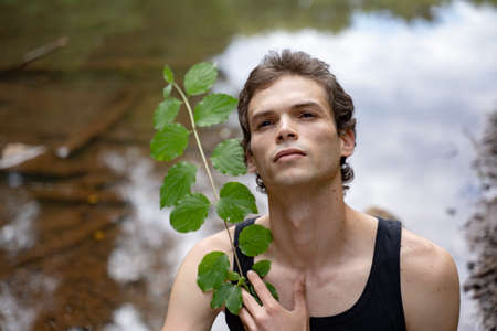 Close-up of thoughtful man holding plant against lake in forestの写真素材