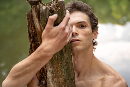Close-up portrait of shirtless serious man embracing wood in forestの写真素材