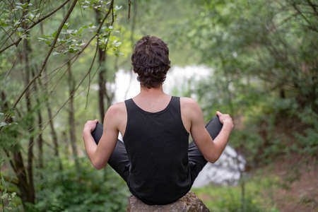Rear view of man sitting on rock against trees in forestの写真素材