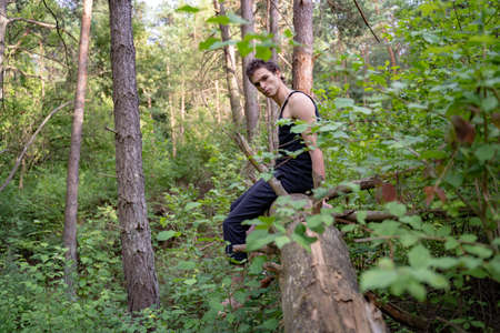 Side view portrait of serious man sitting on log against trees in forestの写真素材