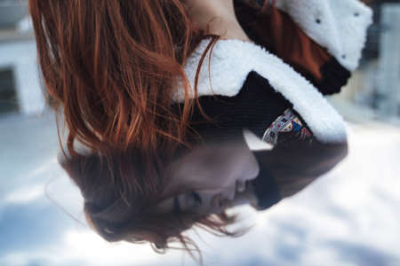 Mirror reflection of female model face with head tilted back and closed eyes. Beautiful red haired young woman enjoying evening outdoors.の写真素材