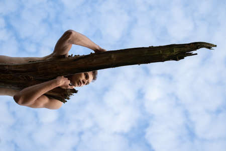 Low angle view of thoughtful man looking away while lying on log against cloudy sky in forestの写真素材