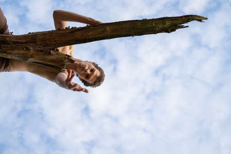Low angle portrait of man showing hand while lying on log against cloudy sky in forestの写真素材