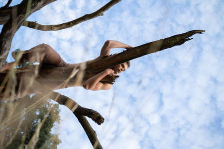 Low angle view of thoughtful man lying on log against cloudy sky in forestの写真素材