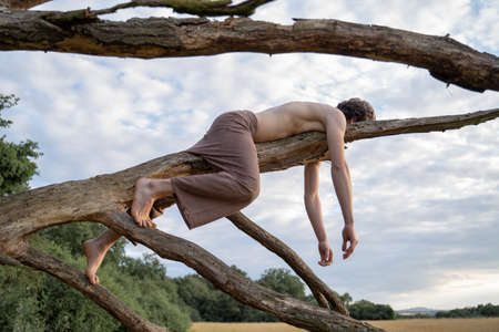Side view of shirtless man lying on log against sky in forestの写真素材