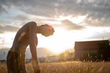 Side view of shirtless man standing amidst plants against cloudy sky in forest at sunsetの写真素材