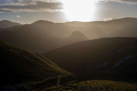 Scenic view of sun shining over mountains against skyの写真素材