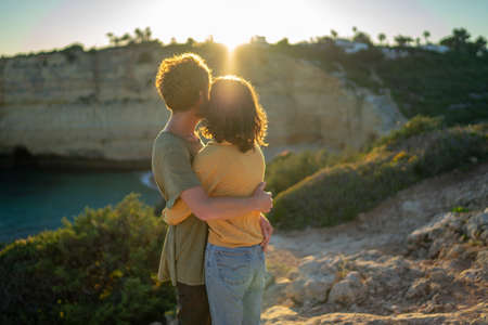 Side view of mid adult couple embracing while standing on cliff during sunsetの写真素材