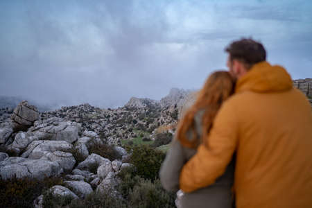 Rear view of couple looking at mountain against cloudy skyの写真素材