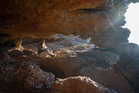 Side view of woman sitting on rock formation at beach during sunsetの写真素材