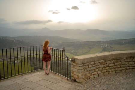 Rear view of woman looking at view while standing by railing on observation point during sunsetの写真素材