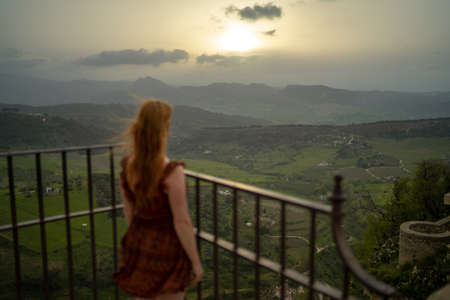 Rear view of woman looking at mountains while standing on observation point during sunsetの写真素材