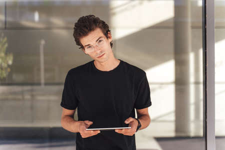 Portrait of confident young man in black t-shirt holding tablet computer outside officeの写真素材