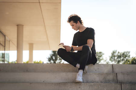 Full length of young male university student using digital tablet while sitting at campusの写真素材