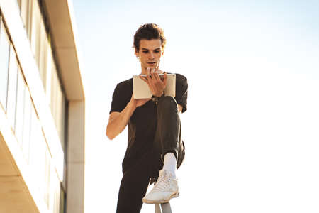 Handsome young man using digital tablet while sitting on railing against clear sky