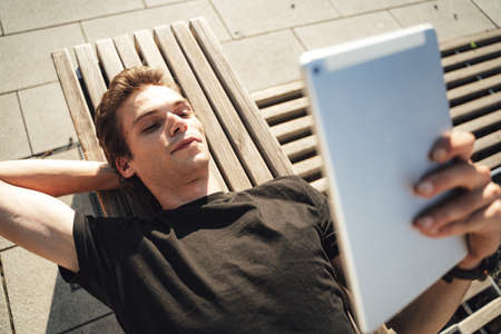 Directly above shot of college student studying online on digital tablet while lying on bench at campusの写真素材