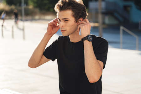 Handsome young man putting on earbuds to listen music at college campusの写真素材