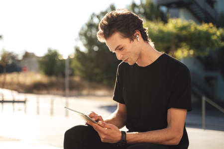 Young Caucasian man using digital tablet while sitting at university campus on sunny day