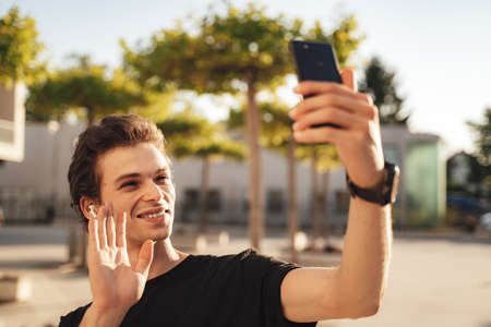 Caucasian young man waving hand while having video call on smartphone at campusの写真素材