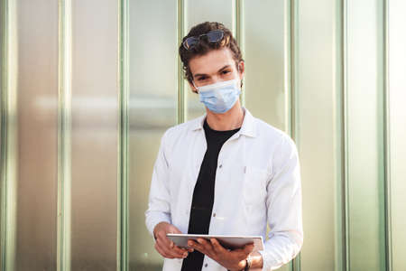 Portrait of confident doctor wearing face mask while holding digital tablet against wall during COVID-19 outbreakの写真素材