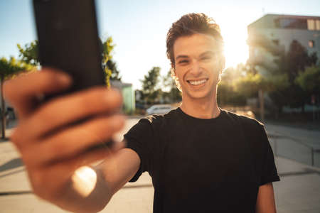 Smiling European man taking selfie through mobile phone in city on sunny dayの写真素材