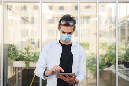 Caucasian male researcher wearing face mask while using digital tablet at greenhouseの写真素材