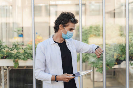 Agronomy scientist holding digital tablet while watching time at glasshouse during COVID-19 outbreakの写真素材