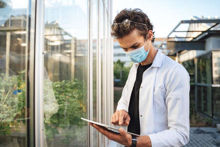 Young male scientist using digital tablet to analyze plants in greenhouseの写真素材