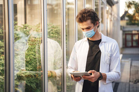 Young male scientist monitoring plant development with digital tablet in glasshouse during COVID-19 outbreakの写真素材