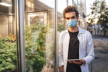 Portrait of a male Caucasian scientist with digital tablet working at greenhouse during COVID-19 outbreakの写真素材