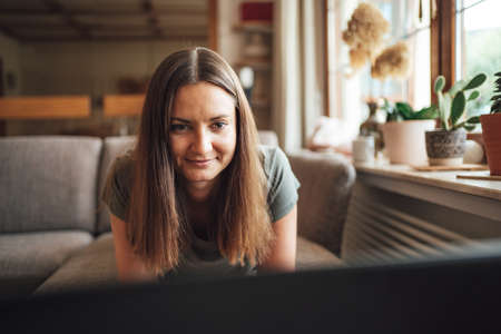Attractive brunette woman having conference call on laptop in living room at homeの写真素材