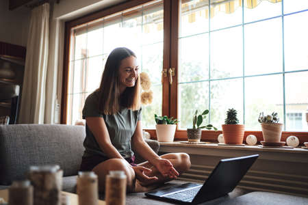 Cheerful European woman video conferencing with friend on laptop at homeの写真素材